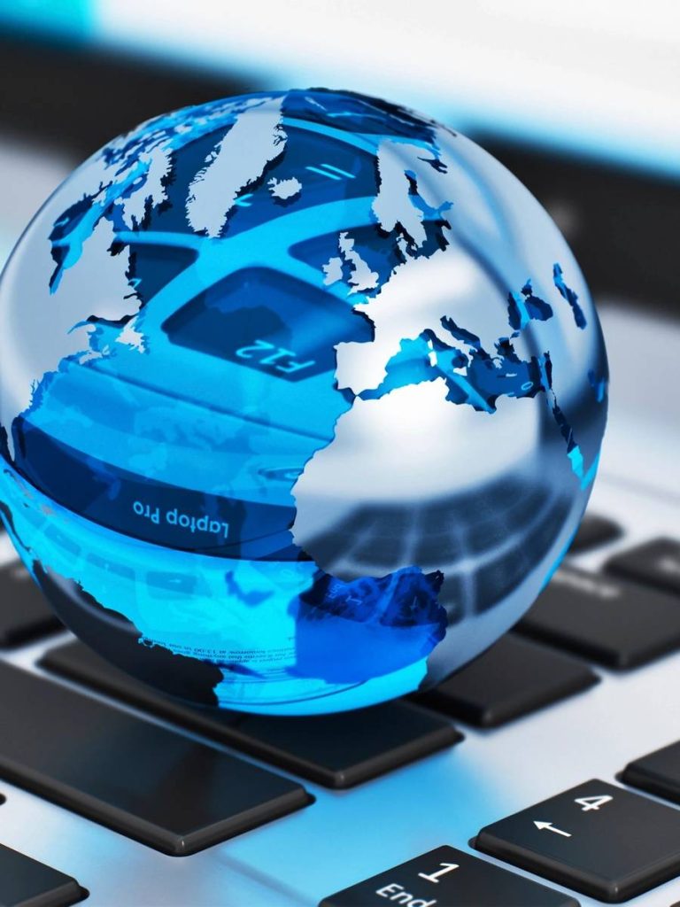 A blue, translucent globe rests on a laptop keyboard, symbolizing global connectivity and technology.