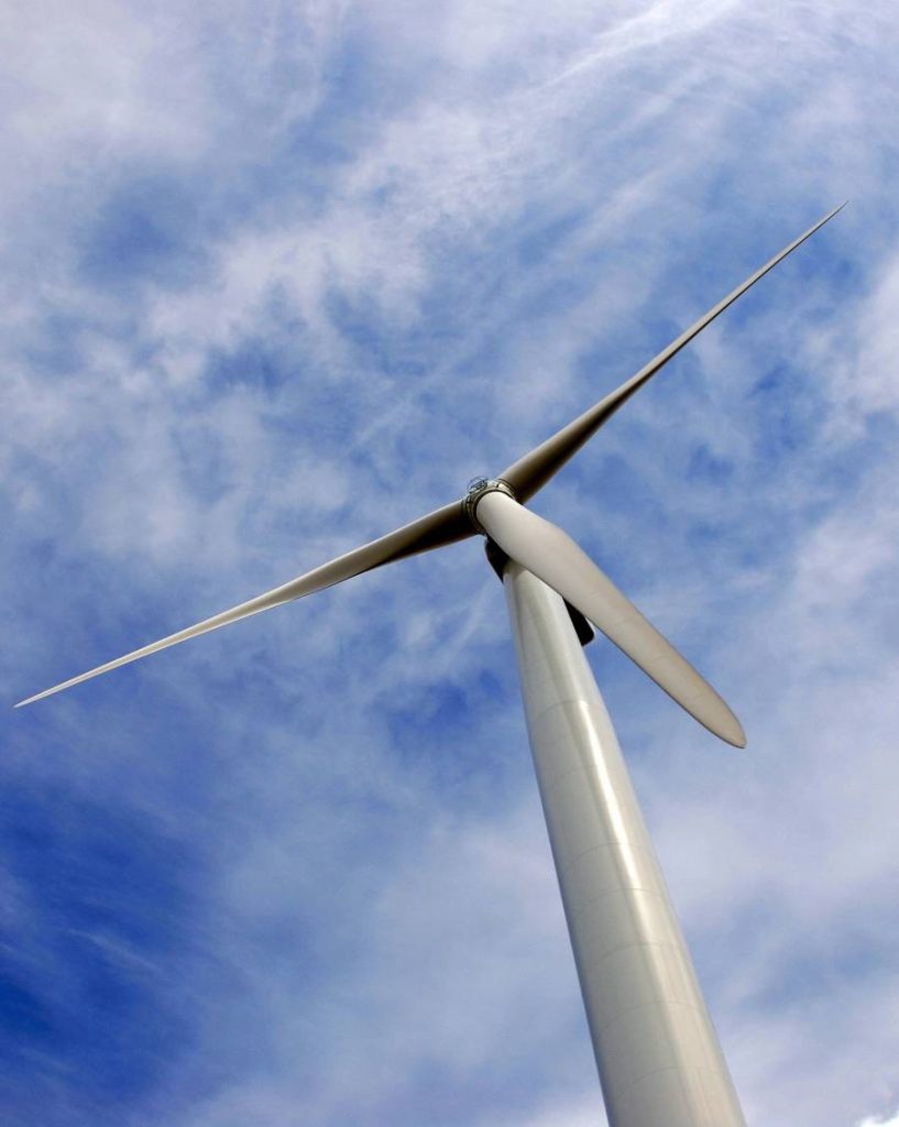 A low-angle view of a wind turbine against a blue sky with clouds.